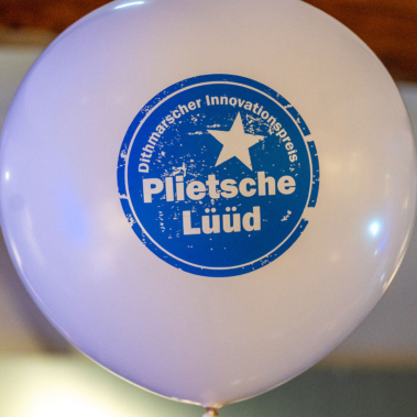 Ein weißer Ballon mit blauem Aufdruck: "Dithmarscher Innovationspreis" und "Plietsche Lüüd" um einen zentralen Stern. Der Hintergrund ist unscharf.